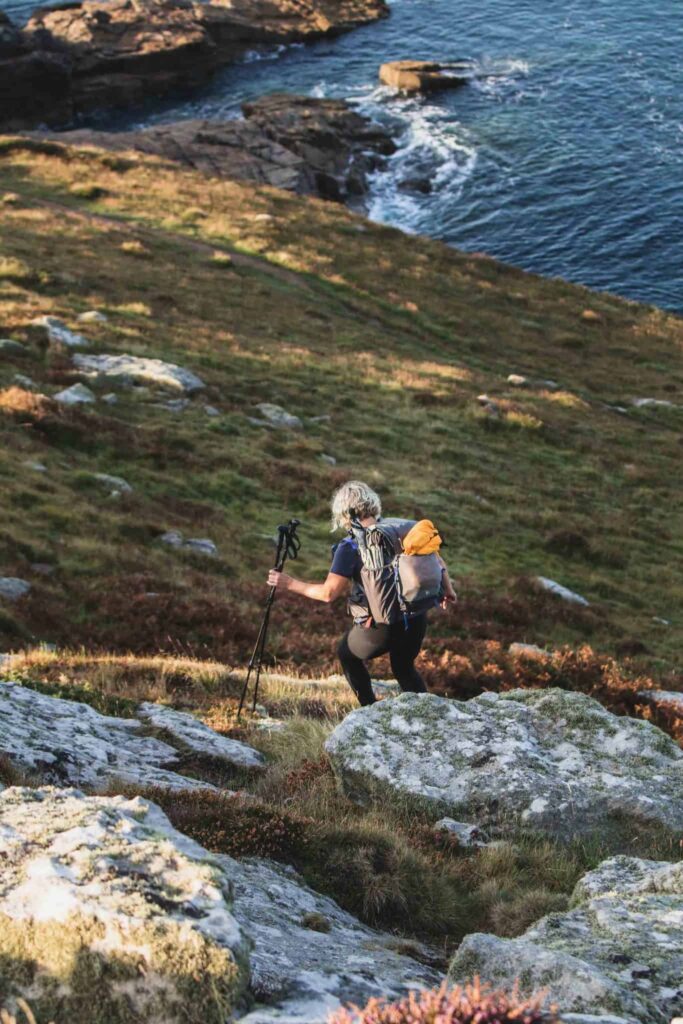 Gail going downhill away from the camera in her backpack surrounded by rocks and heather.