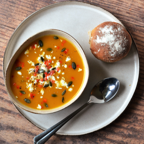 Butternut squash, pear and leek soup on a plate with a bread roll and spoon