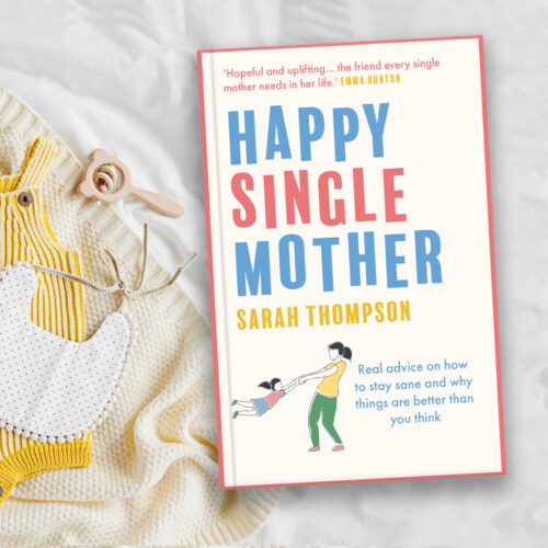 Happy Single Mother book lying flat on white bedding next to yellow baby grow