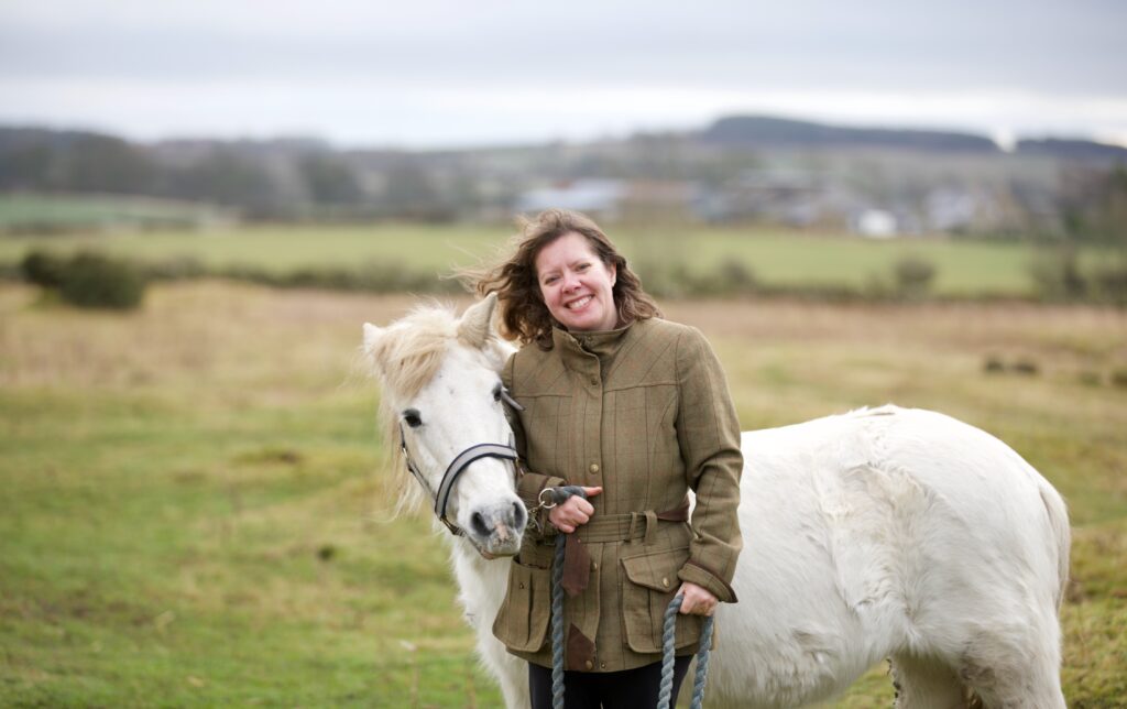 Sally stands in a field with a white pony.