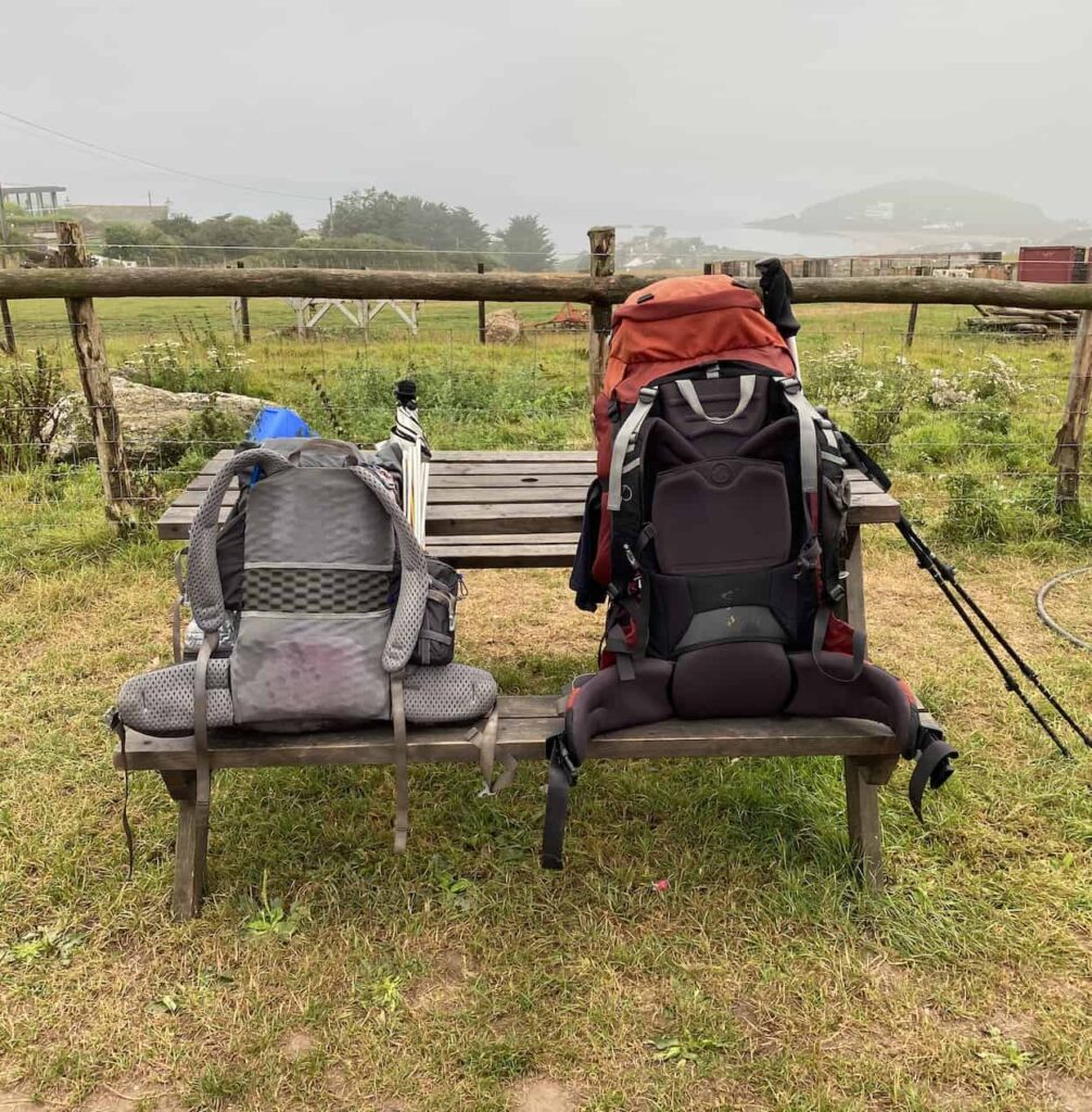 Two backpacks on a picnic bench with some hiking poles on a misty day