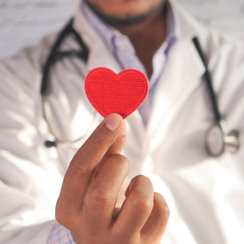 Red heart in foreground, held by a person wearing a lab coat and stethoscope in the background